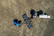 Вид с воздуха фермера, заполняющего бункер с сеялкой воздуха грузовиком в поле с голубым небом на заднем плане — стоковое фото
