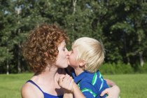 Madre sosteniendo y besando a su joven hijo - foto de stock