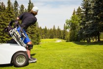 Un golfeur physiquement handicapé qui utilise un fauteuil roulant spécialisé pour décoller et conduire une balle sur le fairway d'un terrain de golf, Edmonton, Alberta, Canada — Photo de stock