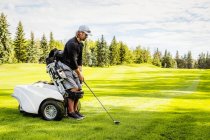 Гольфист с ограниченными физическими возможностями, использующий специализированную инвалидную коляску, выстроил своего водителя с мячом на зеленом поле для гольфа, Эдмонтон, Альберта, Канада — стоковое фото