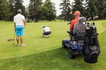 Дві можливості здорові гольфістів об'єднатися з обмеженими гольфіста за допомогою спеціалізованих енергії гольф візку і покласти разом на гольф green грає кращий м'яч, Едмонтон, Альберта, Канада — стокове фото
