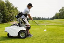 Un golfista con discapacidad física que conduce una pelota en un campo de golf y utiliza una silla de ruedas hidráulica motorizada especializada en asistencia de golf, Edmonton, Alberta, Canadá - foto de stock
