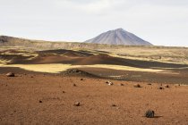 Um campo vulcânico marrom leva o olho para um pico vulcânico na distância, com a cratera do vulcão visível, Malargue, Mendoza, Argentina — Fotografia de Stock