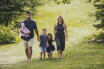 Una madre e un padre in un matrimonio misto corsa a piedi con i loro figli in un parco su una gita in famiglia durante una calda giornata autunnale — Foto stock