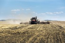 Tractor pulling an air seeder, seeding a field with blue sky and clouds in the background — Stock Photo