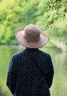 Mulher com um chapéu de aba olhando para um lago tranquilo; Northumberland, Inglaterra — Fotografia de Stock