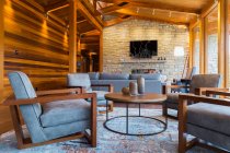 Braune hölzerne und graue gepolsterte Sitzstühle, runder Tisch und Sofas mit Natursteinkamin im Wohnbereich des großen Raumes — Stockfoto