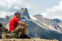 Male hiker sitting on a rocky area overlooking mountain vista in the background; British Columbia, Canada — Stock Photo