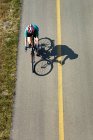 Vista aérea mirando hacia abajo a una ciclista femenina en una ruta pavimentada con sombra de ciclista; Calgary, Alberta, Canadá - foto de stock