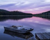 Wooden rowboat beside a dock on a tranquil lake reflecting the pink of a sunset, Lac Le Jeune Provincial Park; Kamloops, British Columbia, Canada — Stock Photo