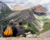 Männliche und weibliche Wanderer sitzen auf einem Felsgrat mit Blick auf ein Tal und eine Bergkette im Kananaskis Country; Alberta, Kanada — Stockfoto