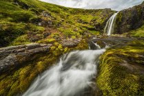 Água caindo de penhasco rochoso para um riacho abaixo; Islândia — Fotografia de Stock