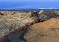 Estrada sinuosa através do Parque Nacional de Timanfaya mostrando fissuras de rocha vulcânica com oceano ao fundo, Lanzarote, Espanha — Fotografia de Stock