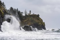 Surf fills the air with salt spray at Cape Disappointment with a lighthouse up on the ridge; Ilwaco, Washington, United States of America — Stock Photo