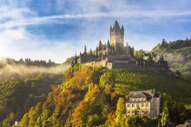 Large medieval castle on a colourful treed hillside with fog, blue sky and clouds, Cochem, Germany — Stock Photo