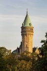 Grande torre de relógio de pedra na área arborizada com luz quente do pôr do sol e céu azul; Cidade de Luxemburgo, Luxemburgo — Fotografia de Stock