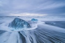 Большой ледяной блок лежит на берегу Южной Исландии, в то время как волны разбиваются на берегу; Исландия — стоковое фото