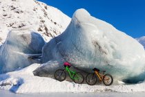 Fatbikes, 907 жировий велосипед на шині і Fatback жировий велосипед, відпочиваючи проти гігантського айсберга взимку на озері Портаж, національний ліс Чугач; Портаж, Аляска, США — стокове фото