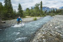 Man fat biking across a stream in Wrangell - St. Elias National Park and Preserve on a cloudy summer day in South-central Alaska, United States of America — Stock Photo