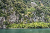 Горные склоны и водопад, Национальный парк Фиордленд, пролив Милфорд; Южный остров, Новая Зеландия — стоковое фото