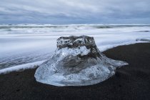 Grande pezzo di ghiaccio seduto sulla riva dell'Islanda con cieli drammatici alle spalle, vicino alla laguna di ghiaccio di Jokulsarlon; Islanda — Foto stock