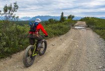 Man fat biking on a dirt road near Eurika on a cloudy summer day in South-central Alaska, United States of America — Stock Photo