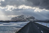 Road leading into the dramatic landscape of Iceland while the sun shines through the clouds making a beautiful scene; Iceland — Stock Photo