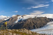 Man hiking near the Harding Icefield Trail with the Kenai Mountains and an unnamed hanging glacier in the background, Kenai Fjords National Park, Kenai Peninsula, South-central Alaska, United States of America — Stock Photo