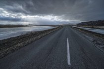 Road leading into the dramatic landscape of Iceland while the sun shines through the clouds making a beautiful scene; Iceland — Stock Photo