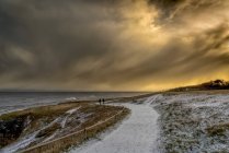 Zwei Gestalten, die in der Abenddämmerung auf dem schneebedeckten Pfad entlang der Küste gehen; Südschilde, Reifen und Verschleiß, England — Stockfoto