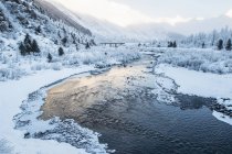 Fluss, der bei Sonnenaufgang durch eine verschneite, bergige Landschaft fließt; alaska, vereinigte Staaten von Amerika — Stockfoto