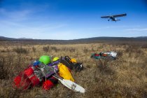 Самолет Буша взлетает с удаленной полосы, с оборудованием для удаленного путешествия в кустах на Аляске на переднем плане; Аляска, Соединенные Штаты Америки — стоковое фото