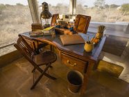 Desk in the foyer of a tent surrounded by windows with a view out to a landscape of dry brush and trees; Rajasthan, India — Stock Photo