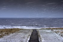 Nevadas tormentosas a lo largo del río Tyne con un camino que conduce al borde del agua y la nieve en la hierba, South Shields, Tyne and Wear, Inglaterra - foto de stock