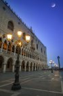 Dogenpalast in der Abenddämmerung mit beleuchteten Laternenpfählen und einem Mond am blauen Himmel; Venedig, Italien — Stockfoto