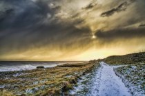 Schneebedeckter Weg entlang der Küste mit goldenem Sonnenlicht, das die Wolken erhellt, Südschilder, Reifen und Verschleiß, England — Stockfoto