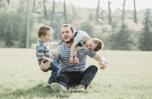 Père avec de jeunes fils jouant dans un parc ; Edmonton, Alberta, Canada — Photo de stock