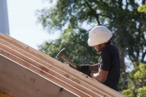 Carpenter hammering on roof rafters at building construction site — Stock Photo