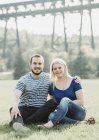 Retrato de casal em um parque sentado na grama com uma ponte no fundo; Edmonton, Alberta, Canadá — Fotografia de Stock