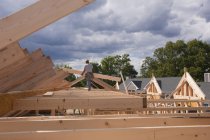 Carpenter putting up roof rafters at building construction site — Stock Photo