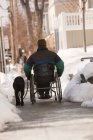 Mulher com esclerose múltipla em uma cadeira de rodas com um cão de serviço na neve de inverno — Fotografia de Stock
