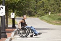 Человек с травмой спинного мозга в инвалидной коляске пересекает доступную улицу — стоковое фото