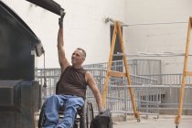 Loading dock worker with spinal cord injury in a wheelchair putting a bag in the dumpster — Stock Photo