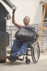 Loading dock worker with spinal cord injury in a wheelchair putting a bag in the dumpster — Stock Photo