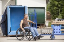 Loading dock worker with spinal cord injury in a wheelchair moving a hand truck — Stock Photo
