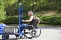 Chargement docker avec lésion de la moelle épinière dans un fauteuil roulant déplacement d'un camion à main — Photo de stock