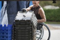 Завантаження працівника док-станції з травмою спинного мозку в інвалідному візку, що рухається складеними інвентарними лотками — стокове фото