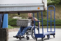 Trabajador portuario de carga con lesión medular en una silla de ruedas moviendo bandejas de inventario apiladas - foto de stock