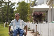 Uomo con lesione del midollo spinale in sedia a rotelle su una passeggiata periferica con case — Foto stock