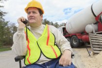 Construction supervisor with Spinal Cord Injury on walkie talkie with concrete mixer truck — Stock Photo